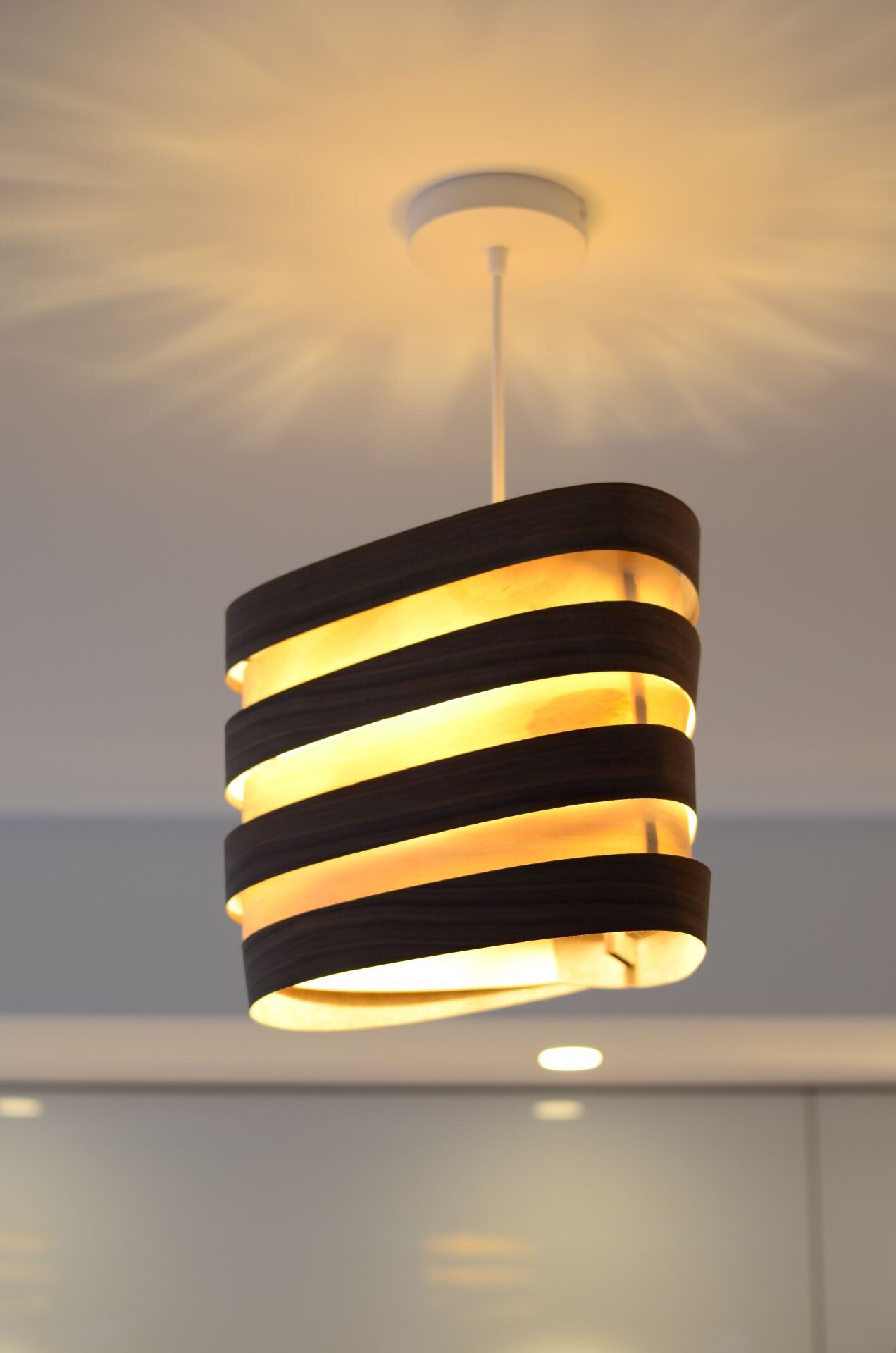Suspensions Nest Duo en bois de bouleau et noyer installées au-dessus d’un îlot de cuisine moderne, lumière douce et naturelle.