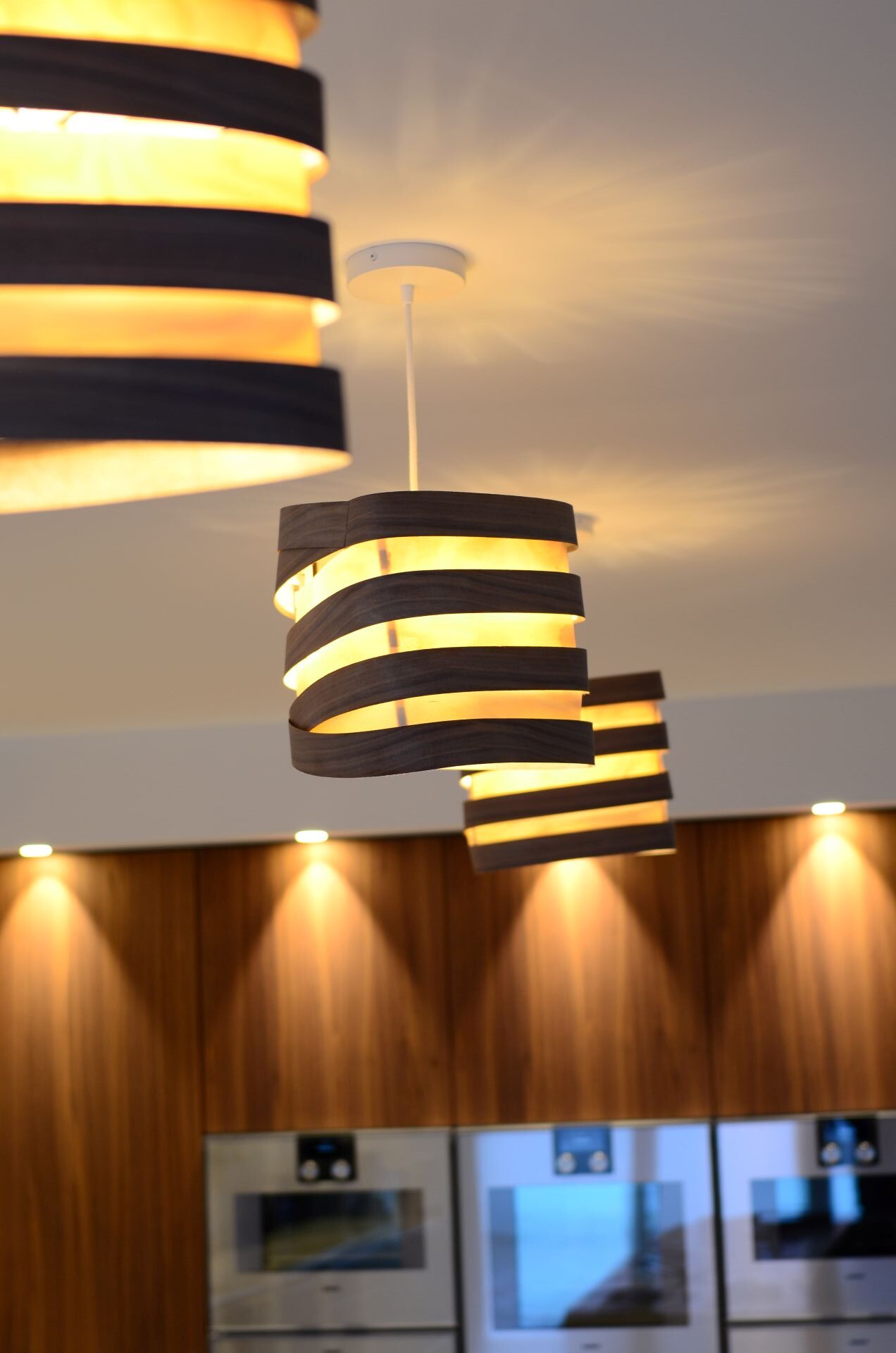 Suspensions Nest Duo en bois de bouleau et noyer installées au-dessus d’un îlot de cuisine moderne, lumière douce et naturelle.