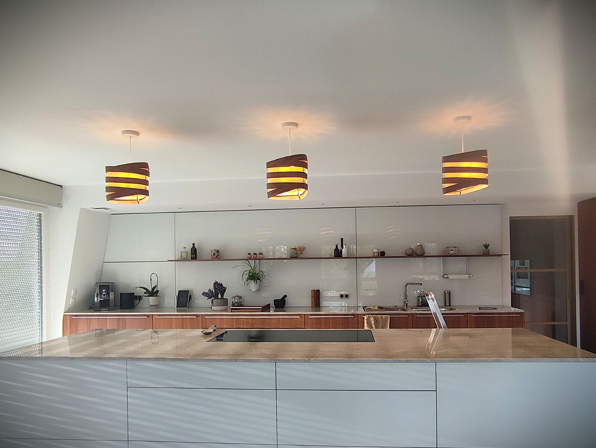 Suspensions Nest Duo en bois de bouleau et noyer installées au-dessus d’un îlot de cuisine moderne, lumière douce et naturelle.