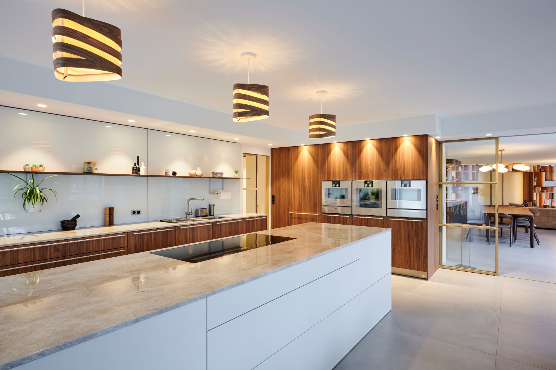 Suspensions Nest Duo en bois de bouleau et noyer installées au-dessus d’un îlot de cuisine moderne, lumière douce et naturelle.