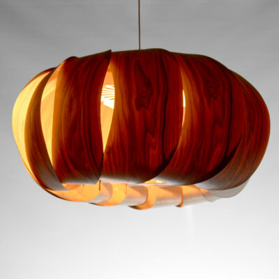 Suspension Poto 2025 en placage bois de noyer, modèle unique Tectoluce, composée de lamelles courbées autour d’une lumière chaude dans un atelier de création.