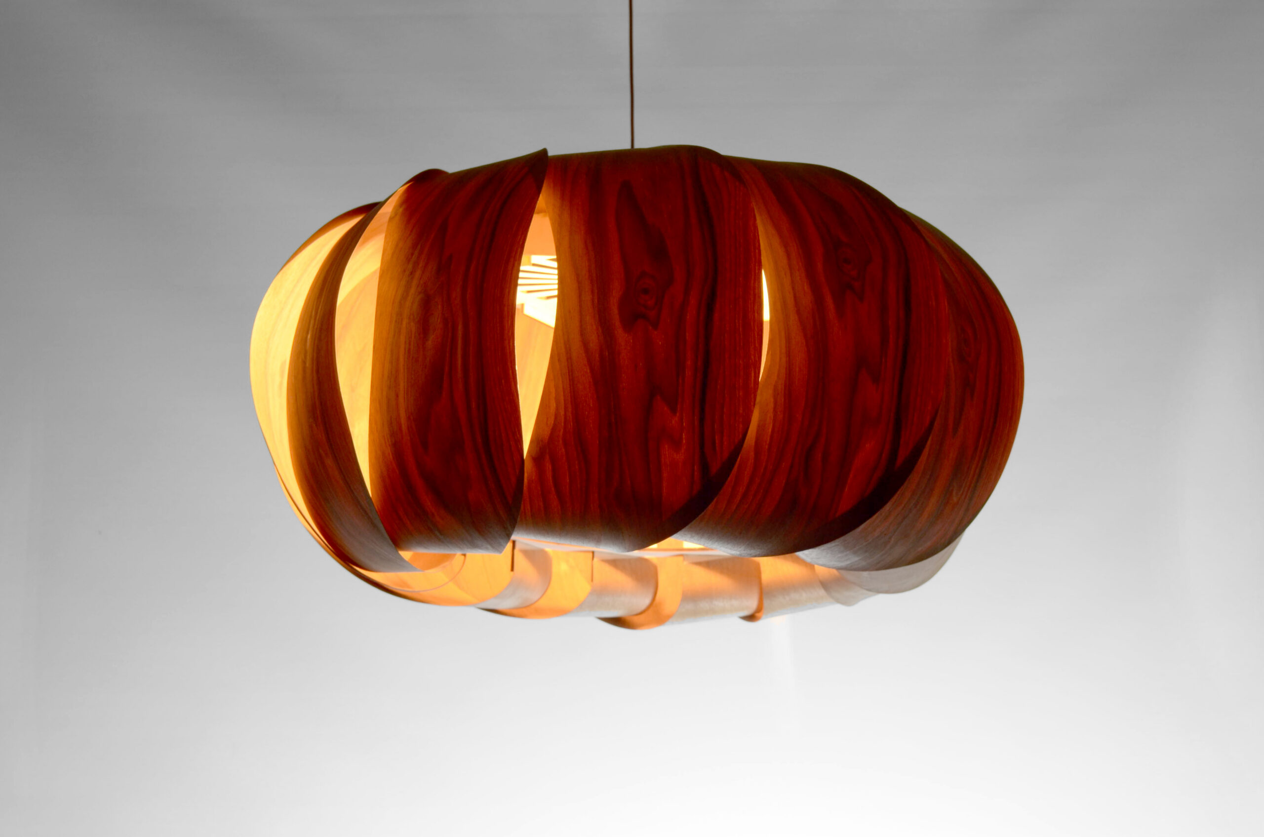 Suspension Poto 2025 en placage bois de noyer, modèle unique Tectoluce, composée de lamelles courbées autour d’une lumière chaude dans un atelier de création.