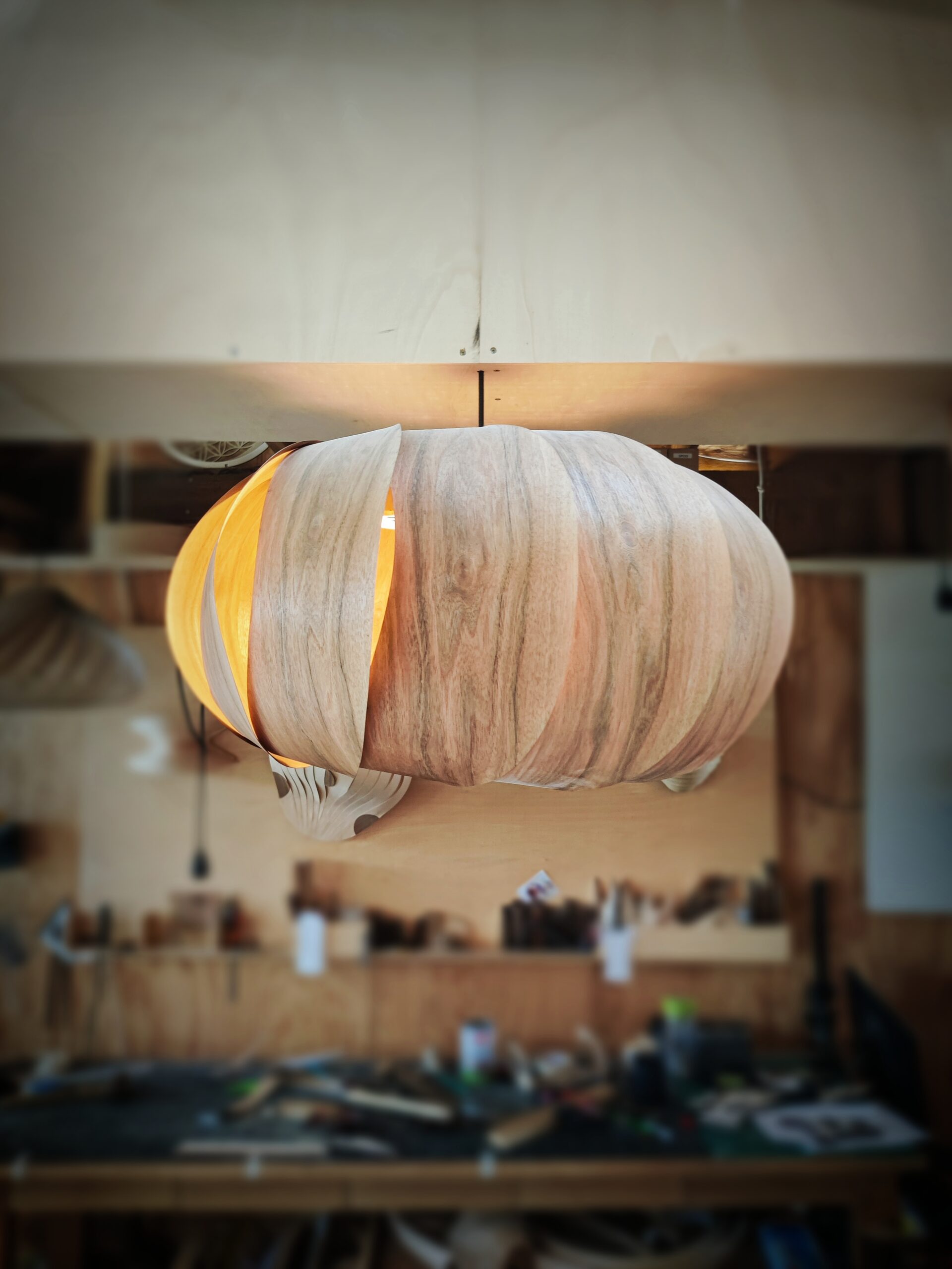 Suspension Poto 2025 en placage bois de noyer, modèle unique Tectoluce, composée de lamelles courbées autour d’une lumière chaude dans un atelier de création.