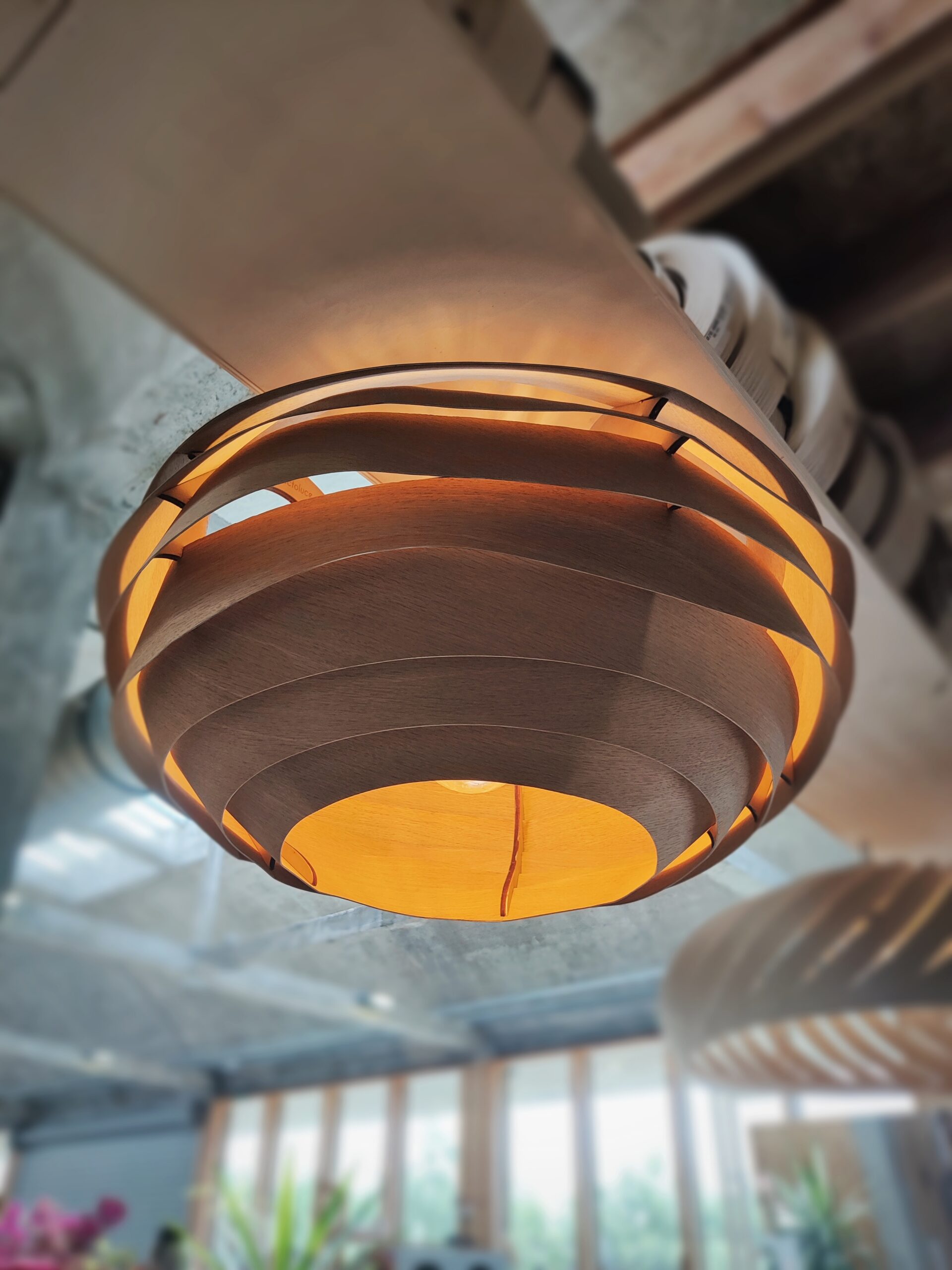 Suspension en bois VESPA, modèle unique Tectoluce, composée de lamelles entrelacées diffusant une lumière chaude dans un atelier de création.