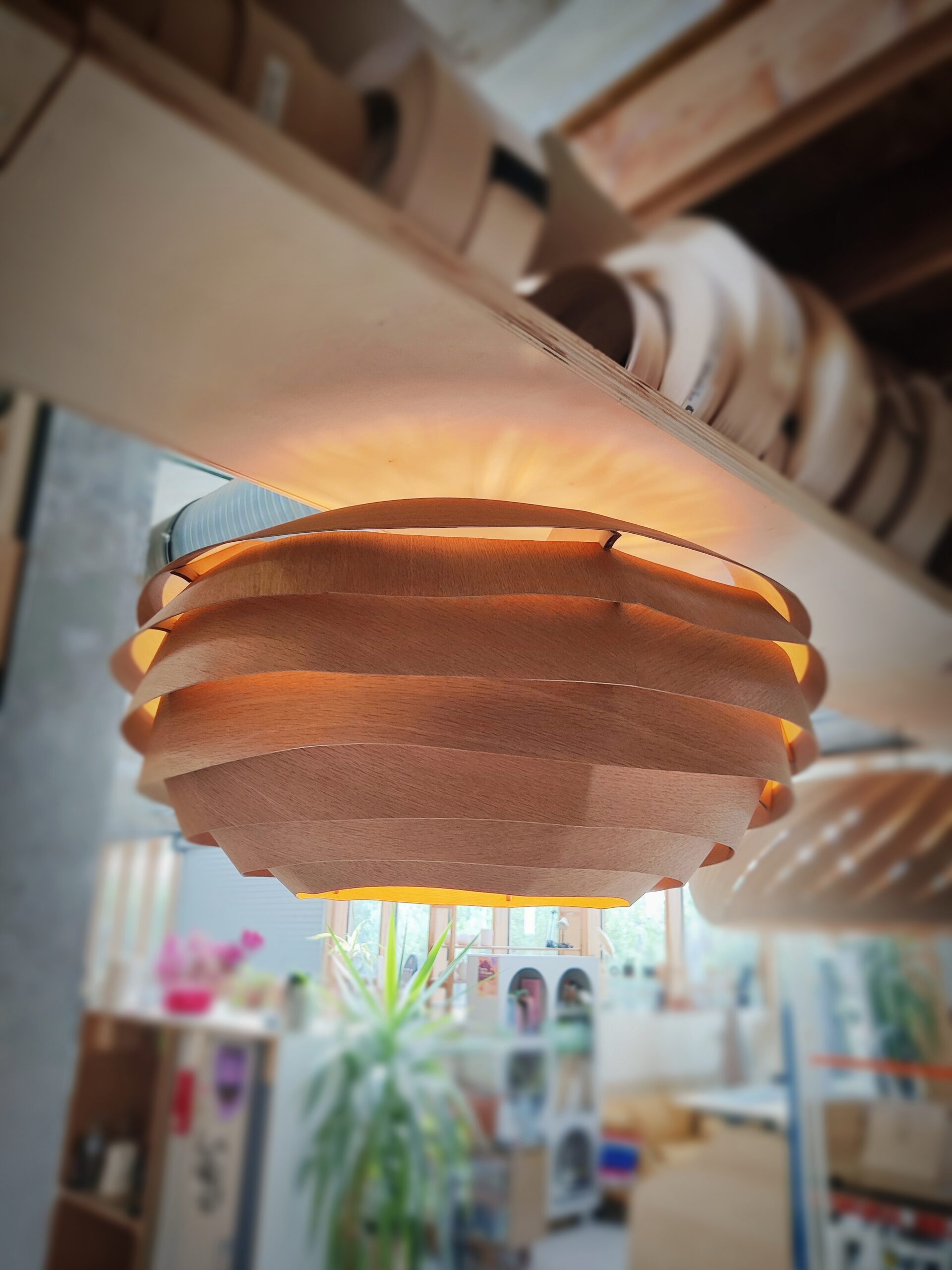 Suspension en bois VESPA, modèle unique Tectoluce, composée de lamelles entrelacées diffusant une lumière chaude dans un atelier de création.