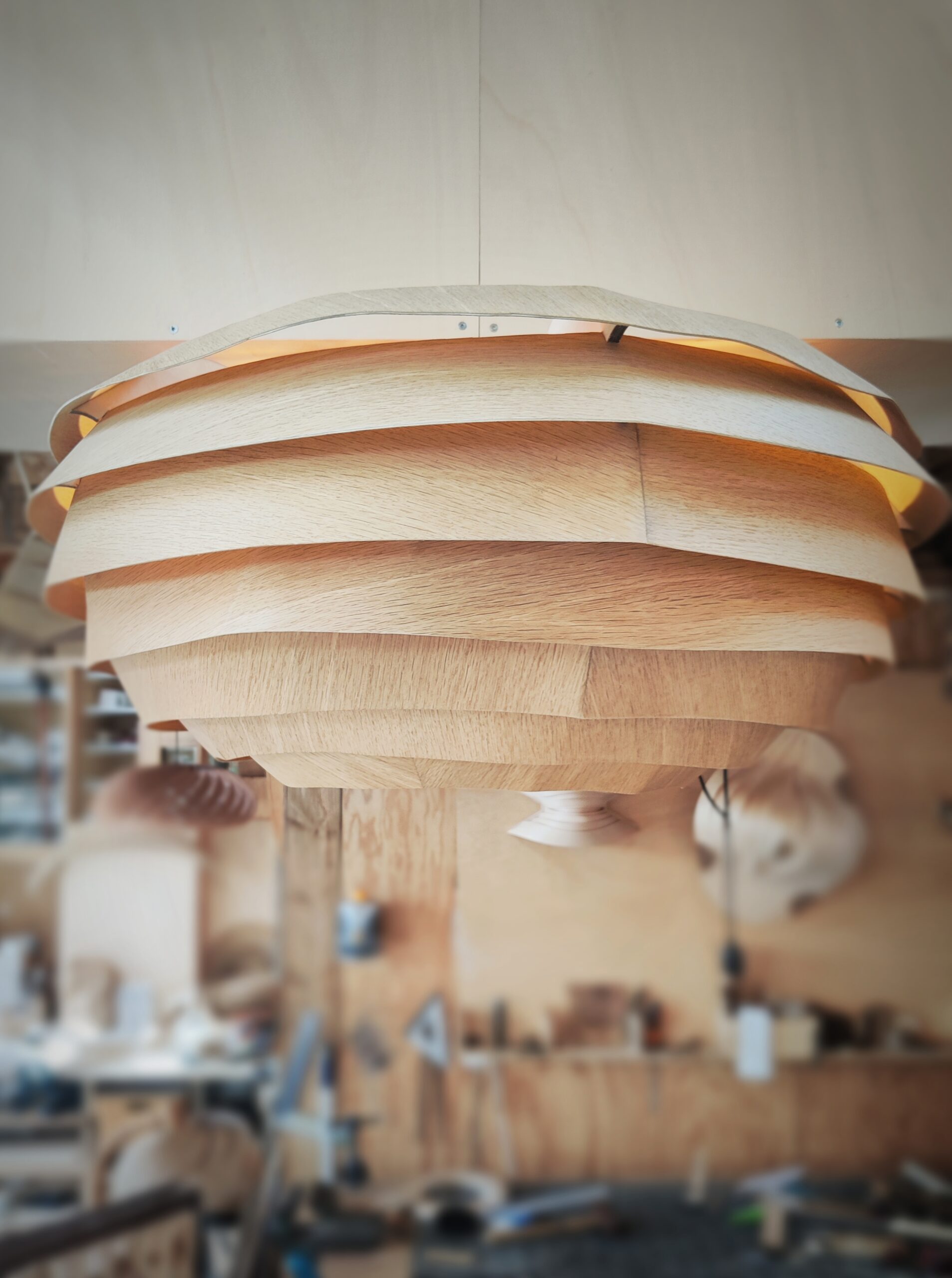Suspension en bois VESPA, modèle unique Tectoluce, composée de lamelles entrelacées diffusant une lumière chaude dans un atelier de création.