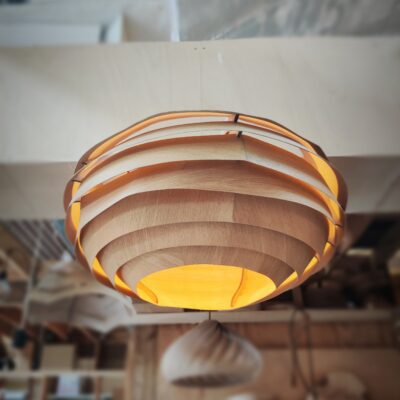 Suspension en bois VESPA, modèle unique Tectoluce, composée de lamelles entrelacées diffusant une lumière chaude dans un atelier de création.
