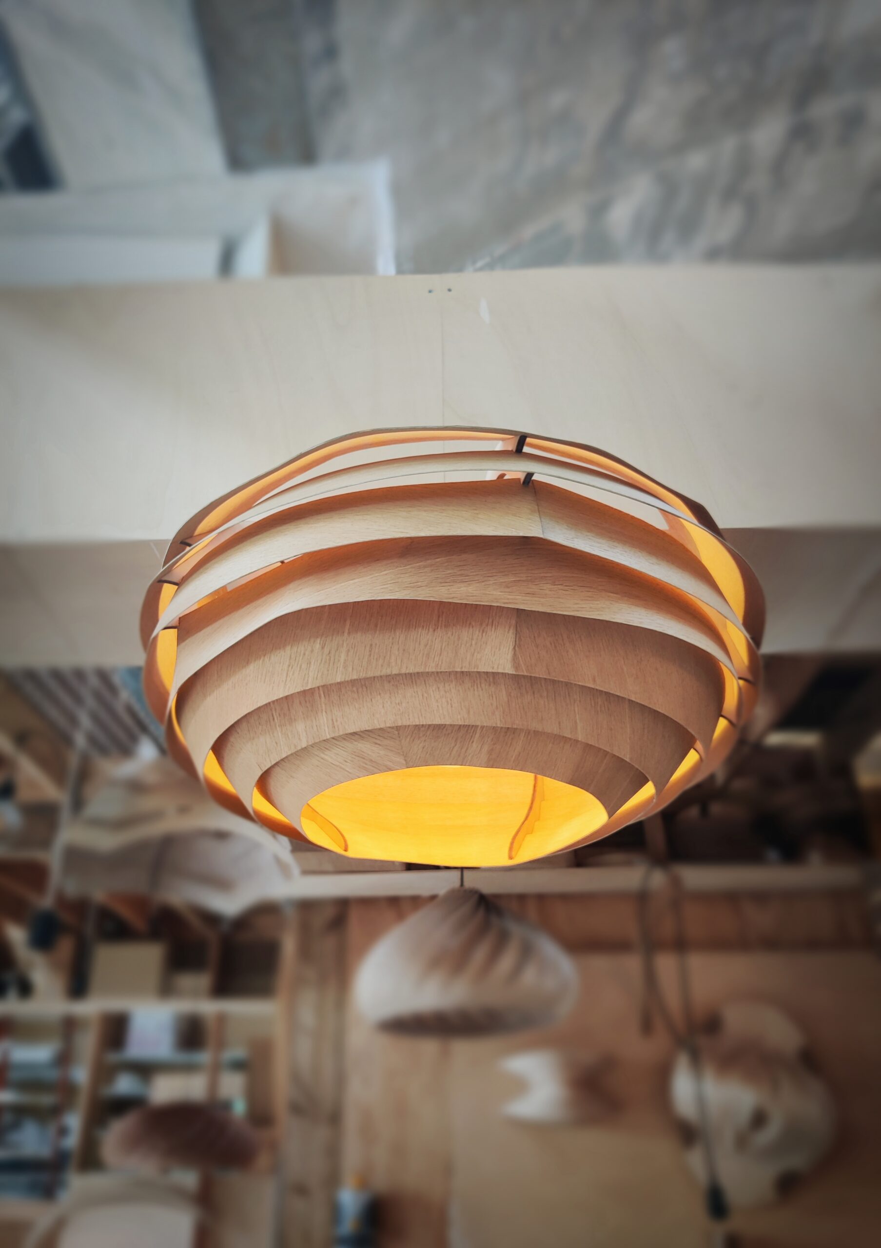 Suspension en bois VESPA, modèle unique Tectoluce, composée de lamelles entrelacées diffusant une lumière chaude dans un atelier de création.